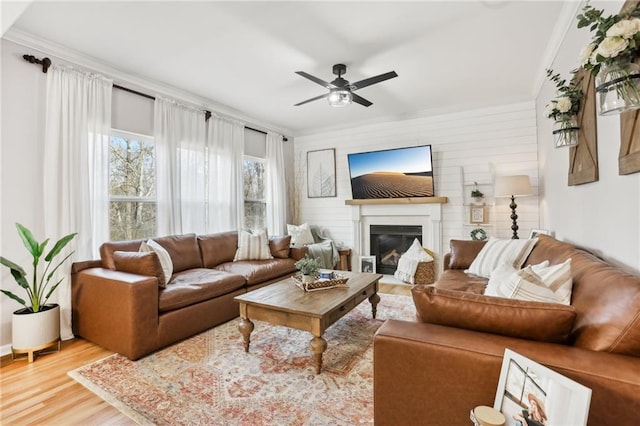 living area featuring crown molding, wood finished floors, a ceiling fan, and a glass covered fireplace