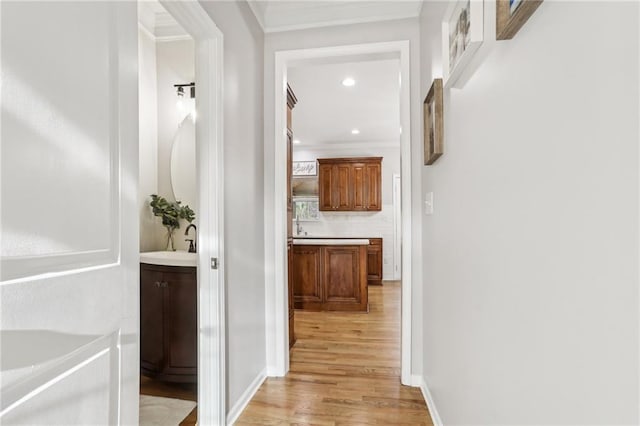 hallway featuring baseboards, ornamental molding, light wood finished floors, and recessed lighting
