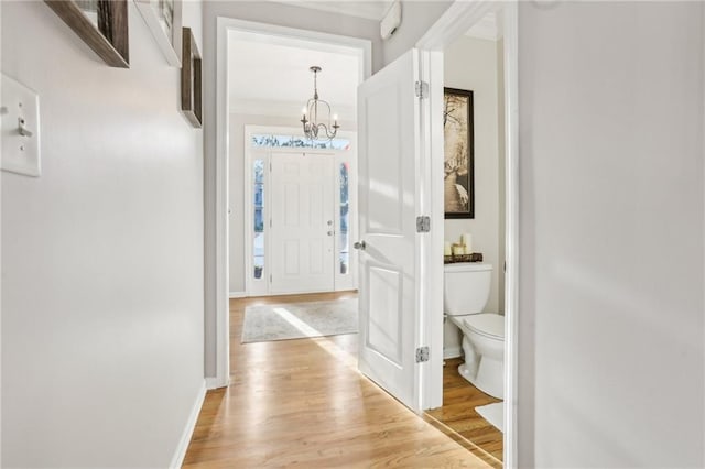 hall with an inviting chandelier, light wood-style floors, and baseboards