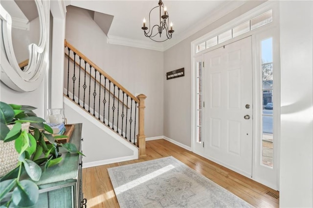 entrance foyer with stairway, an inviting chandelier, ornamental molding, and wood finished floors