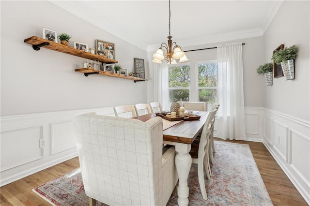 dining room with an inviting chandelier, light wood-style flooring, a wainscoted wall, a decorative wall, and ornamental molding
