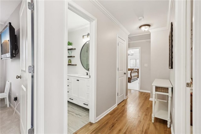 hallway with crown molding, light wood-style flooring, and baseboards