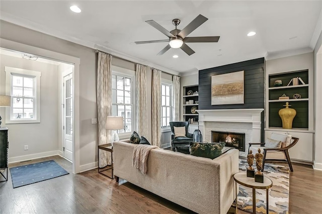 living room with crown molding, baseboards, a lit fireplace, a ceiling fan, and wood finished floors