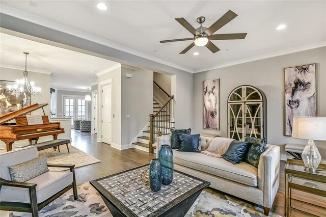 living room featuring stairs, ornamental molding, wood finished floors, and ceiling fan with notable chandelier