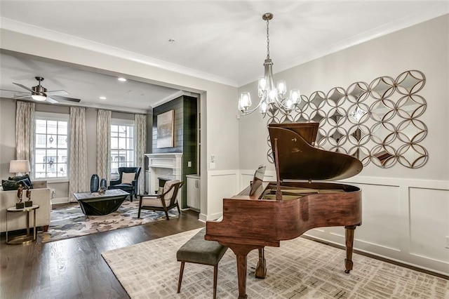 sitting room featuring ceiling fan with notable chandelier, a wainscoted wall, crown molding, and wood finished floors