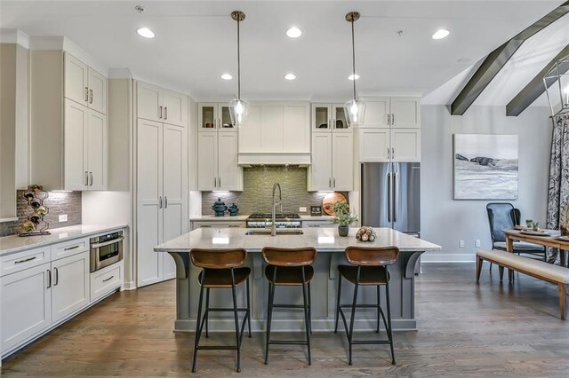 kitchen with a breakfast bar, stainless steel appliances, a center island with sink, glass insert cabinets, and dark wood-style floors
