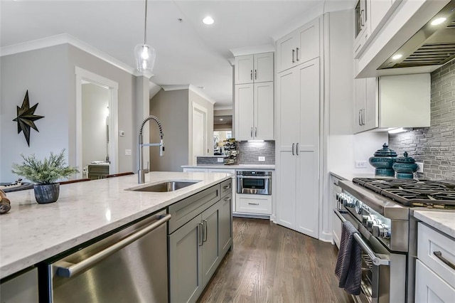 kitchen featuring ornamental molding, appliances with stainless steel finishes, a sink, decorative light fixtures, and exhaust hood