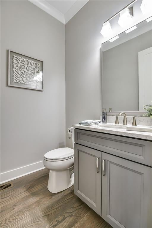 half bath with crown molding, toilet, vanity, wood finished floors, and baseboards