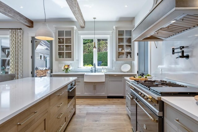 kitchen with sink, tasteful backsplash, pendant lighting, custom range hood, and appliances with stainless steel finishes