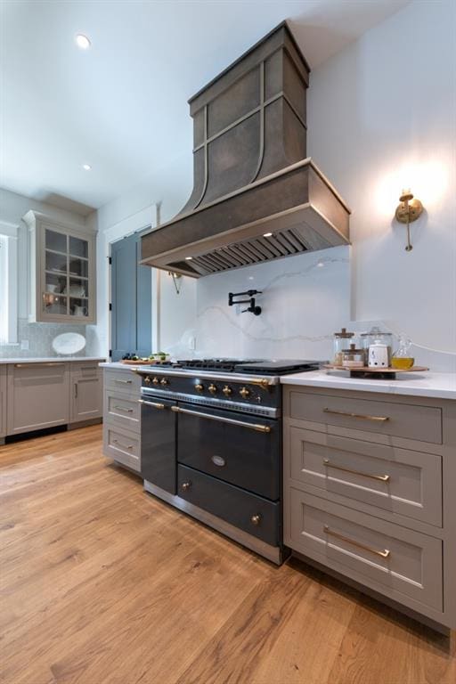 kitchen with premium range hood, tasteful backsplash, high end stainless steel range, and light wood-type flooring