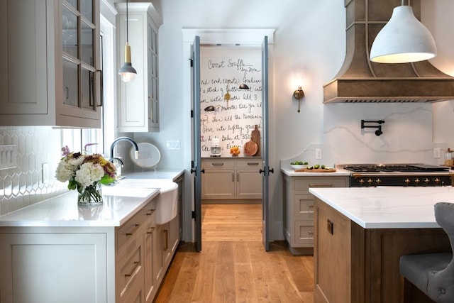 kitchen with premium range hood, tasteful backsplash, range, light hardwood / wood-style floors, and hanging light fixtures