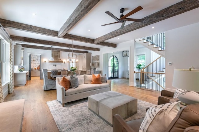 living room with ceiling fan with notable chandelier, light wood-type flooring, and beamed ceiling