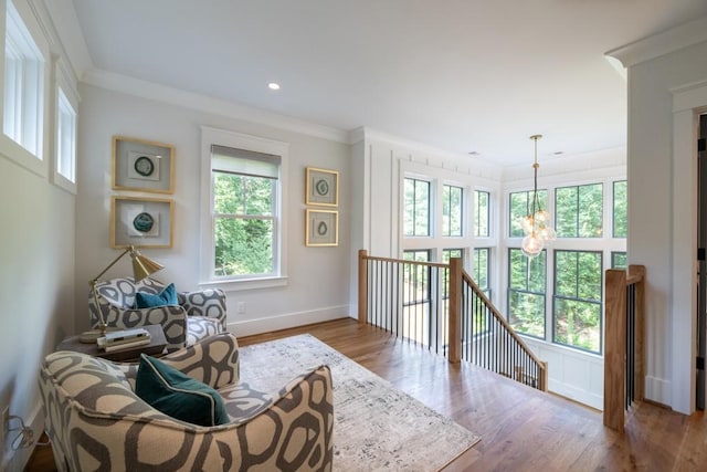 living area featuring plenty of natural light, wood-type flooring, ornamental molding, and an inviting chandelier