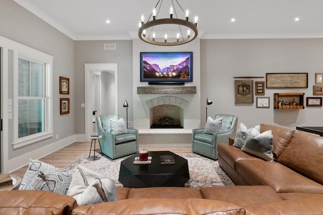 living room with crown molding, a large fireplace, an inviting chandelier, and light wood-type flooring