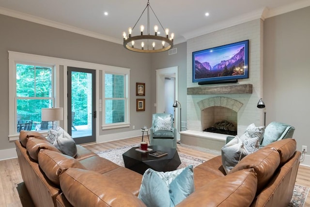 living room featuring a notable chandelier, light wood-type flooring, ornamental molding, and a brick fireplace