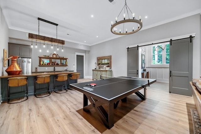 game room with wet bar, a barn door, a chandelier, light hardwood / wood-style floors, and ornamental molding