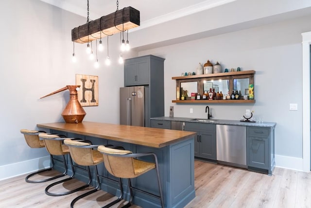 bar featuring sink, hanging light fixtures, stainless steel appliances, light wood-type flooring, and ornamental molding