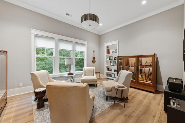 living area with built in shelves, light hardwood / wood-style flooring, and crown molding