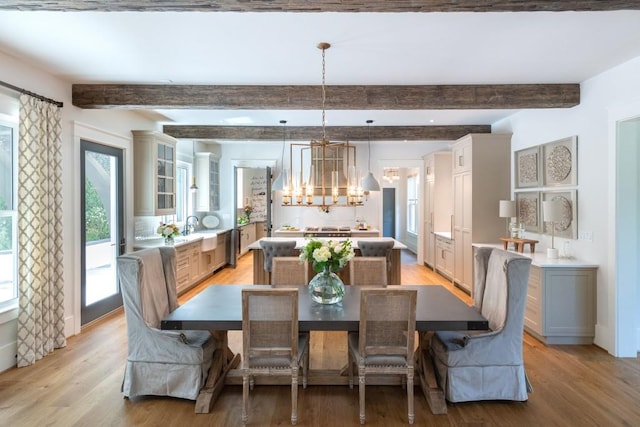 dining space with beamed ceiling, light wood-type flooring, a notable chandelier, and sink