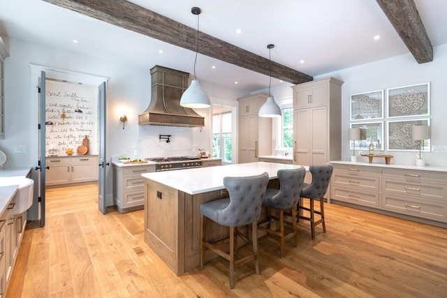 kitchen featuring hanging light fixtures, light hardwood / wood-style floors, a kitchen bar, a kitchen island, and custom exhaust hood