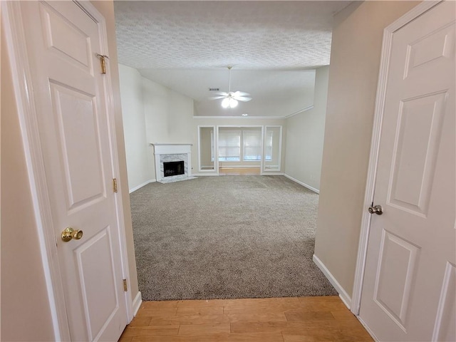 unfurnished living room featuring a premium fireplace, ceiling fan, a textured ceiling, and light hardwood / wood-style flooring