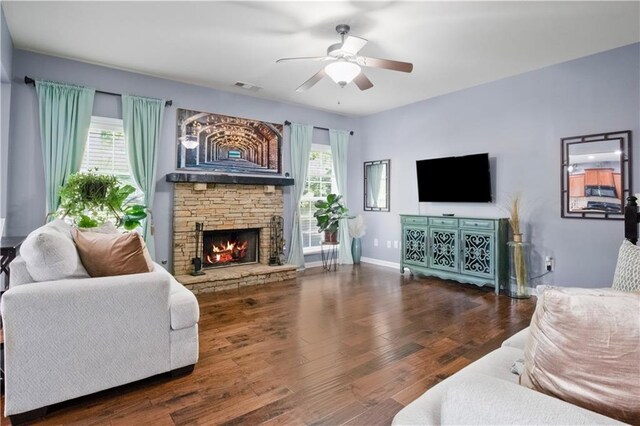 living room featuring a stone fireplace, ceiling fan, plenty of natural light, and dark hardwood / wood-style floors