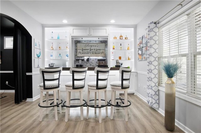 bar with built in shelves, light hardwood / wood-style floors, and white cabinetry