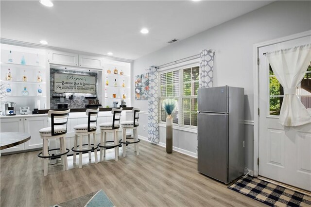 kitchen with built in shelves, stainless steel fridge, a breakfast bar, white cabinets, and light wood-type flooring