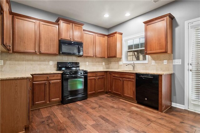 kitchen with black appliances, sink, tasteful backsplash, dark hardwood / wood-style flooring, and light stone counters