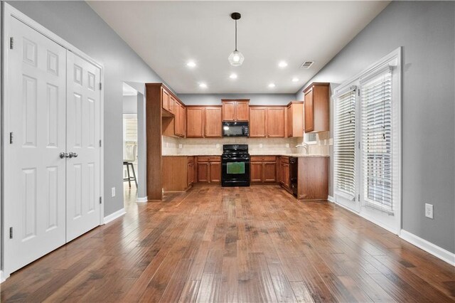 kitchen with backsplash, hanging light fixtures, black appliances, and light hardwood / wood-style floors