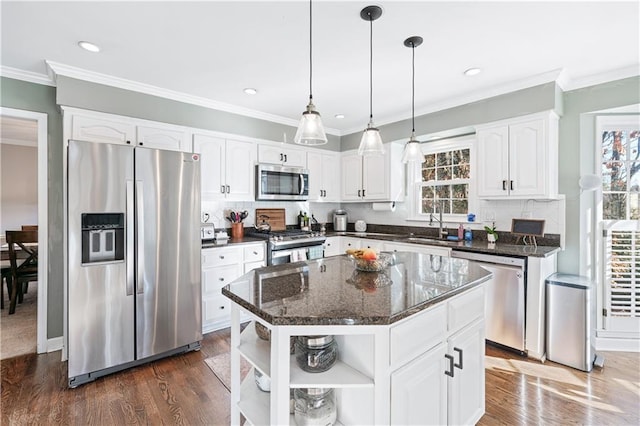 kitchen with appliances with stainless steel finishes, white cabinetry, hanging light fixtures, a center island, and dark stone counters