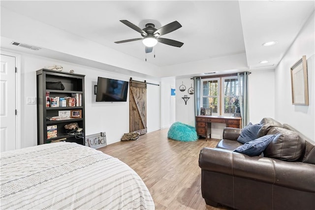 bedroom featuring a barn door, ceiling fan, and light hardwood / wood-style flooring