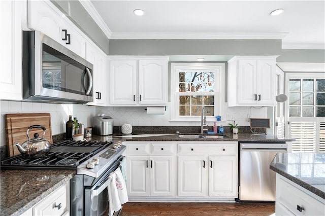 kitchen with appliances with stainless steel finishes, white cabinetry, sink, dark stone counters, and crown molding