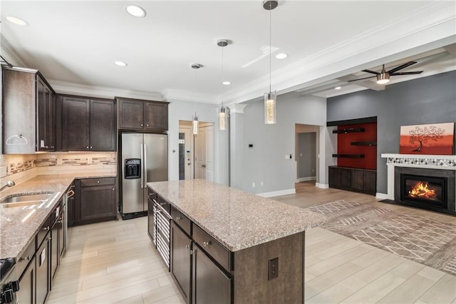 kitchen featuring stainless steel refrigerator with ice dispenser, dark brown cabinetry, light stone counters, a center island, and pendant lighting