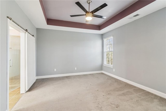 unfurnished room with a barn door, light colored carpet, ceiling fan, and a tray ceiling