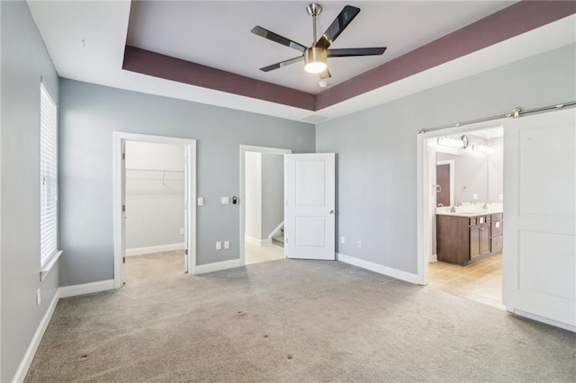 unfurnished bedroom with light carpet, a spacious closet, a raised ceiling, and a barn door