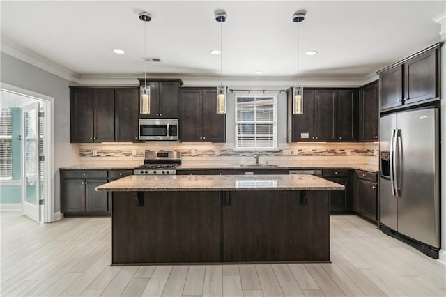 kitchen with light stone counters, hanging light fixtures, stainless steel appliances, and a center island