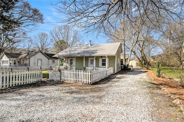 bungalow-style home featuring a fenced front yard, metal roof, driveway, and a porch