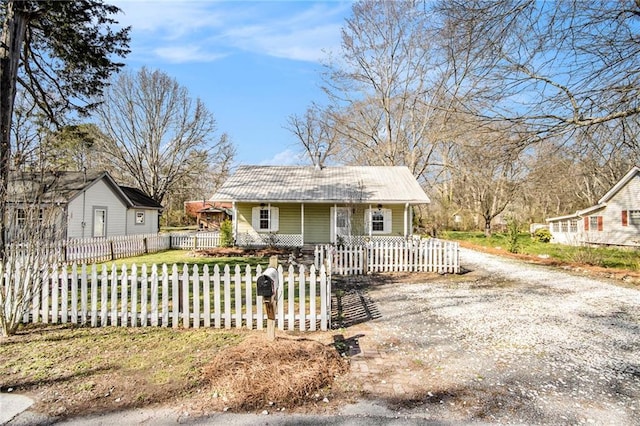 bungalow-style house featuring metal roof, driveway, a porch, and a fenced front yard