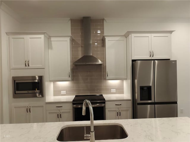 kitchen with stainless steel appliances, a sink, wall chimney range hood, and tasteful backsplash