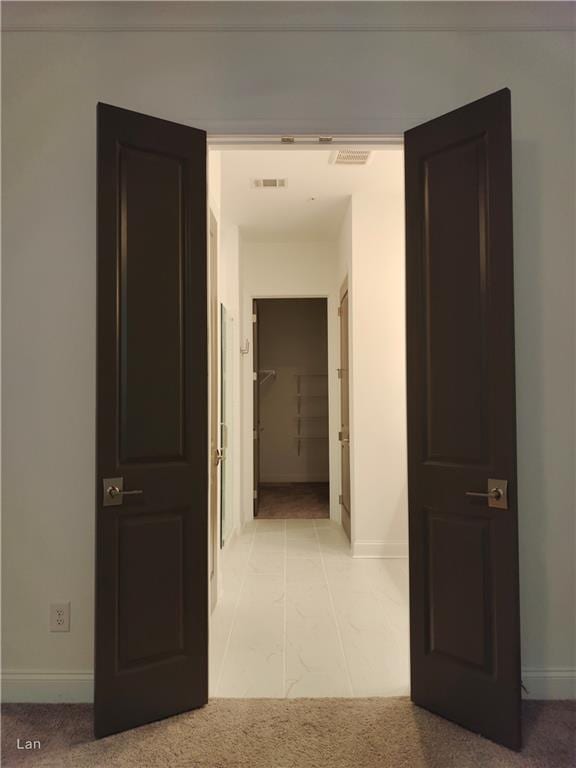 hallway featuring baseboards, visible vents, and light colored carpet