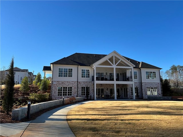 exterior space featuring a balcony, stone siding, a patio area, and a lawn