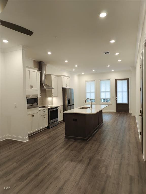 kitchen with visible vents, a kitchen island with sink, stainless steel appliances, wall chimney range hood, and a sink