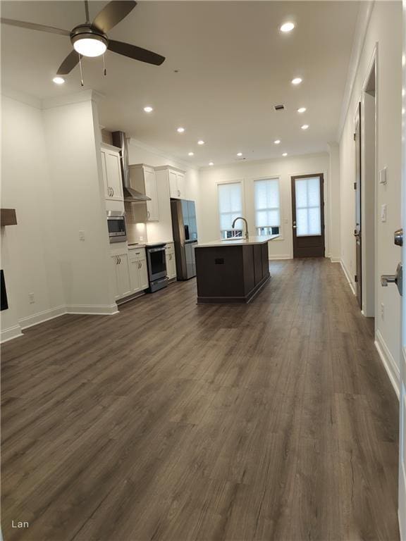 kitchen featuring dark wood-style floors, a center island with sink, appliances with stainless steel finishes, white cabinetry, and wall chimney exhaust hood