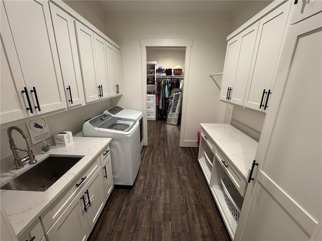 clothes washing area featuring washing machine and clothes dryer, dark hardwood / wood-style flooring, sink, and cabinets