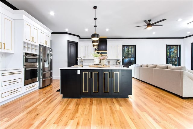 kitchen with an island with sink, stainless steel appliances, pendant lighting, sink, and white cabinetry