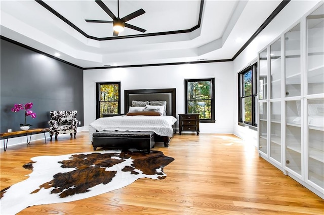 bedroom with a tray ceiling, ornamental molding, multiple windows, and light hardwood / wood-style floors