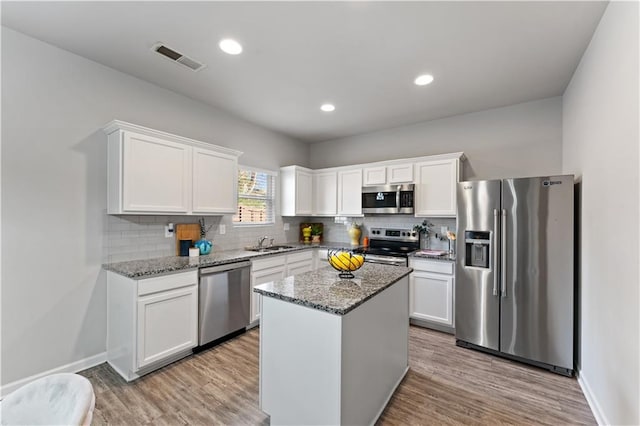 kitchen with white cabinets, a center island, stainless steel appliances, and light stone counters