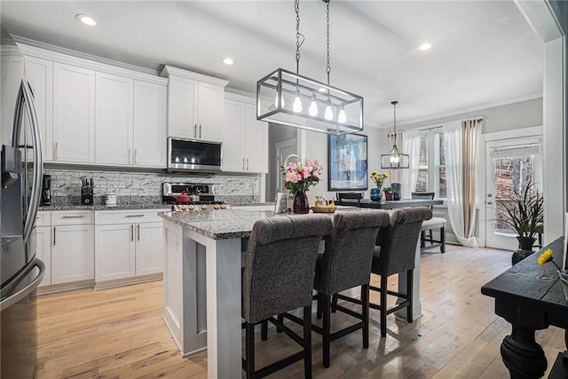 kitchen featuring light stone counters, stainless steel appliances, crown molding, and white cabinetry