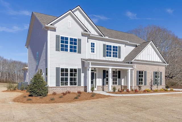 view of front facade with brick siding, board and batten siding, central AC, roof with shingles, and covered porch